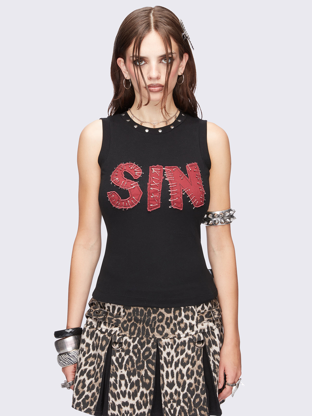 Black vest top featuring a "SIN" red patch with safety pins and studded trim details. 