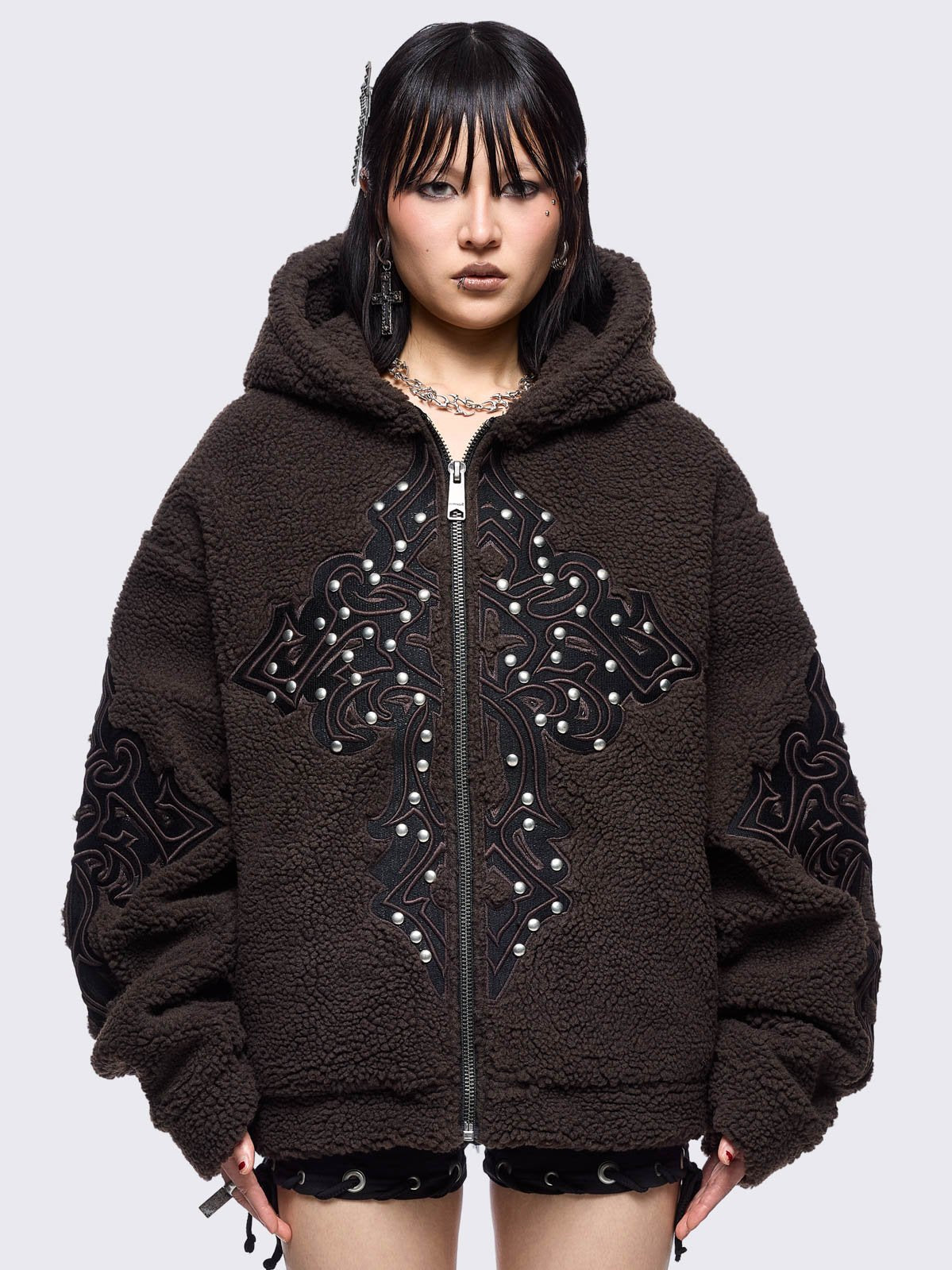Brown fleece hoodie jacket featuring a cross patch on front and sleeves and silver stud details.