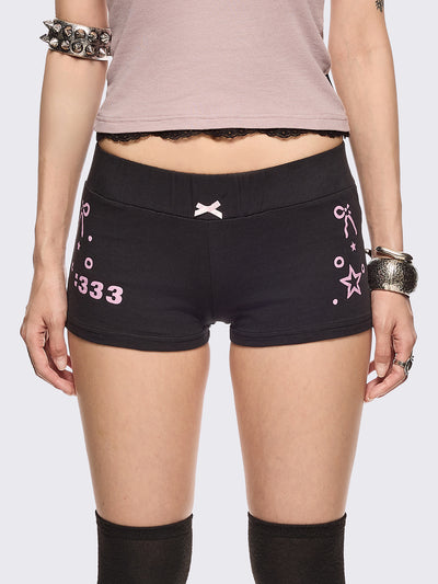 Black sweat micro shorts featuring kaomoji ASCII-style graphic print on side and back and a front pink bow detail. Low rise and elasticized waist.