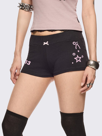 Black sweat micro shorts featuring kaomoji ASCII-style graphic print on side and back and a front pink bow detail. Low rise and elasticized waist.