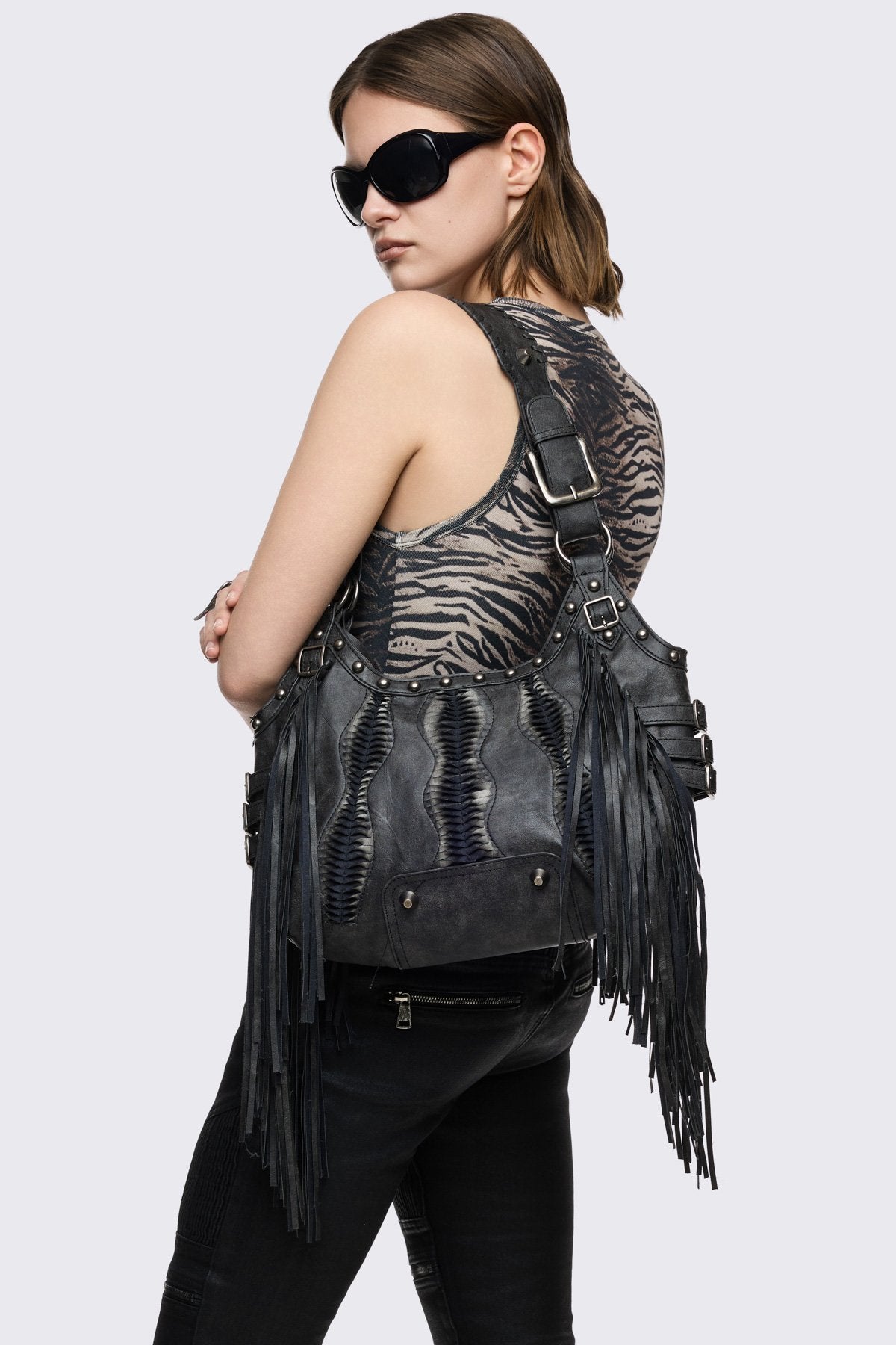 Black faux leather shoulder bag with cascading fringe, buckle and stud details, mini wallet in grunge style.