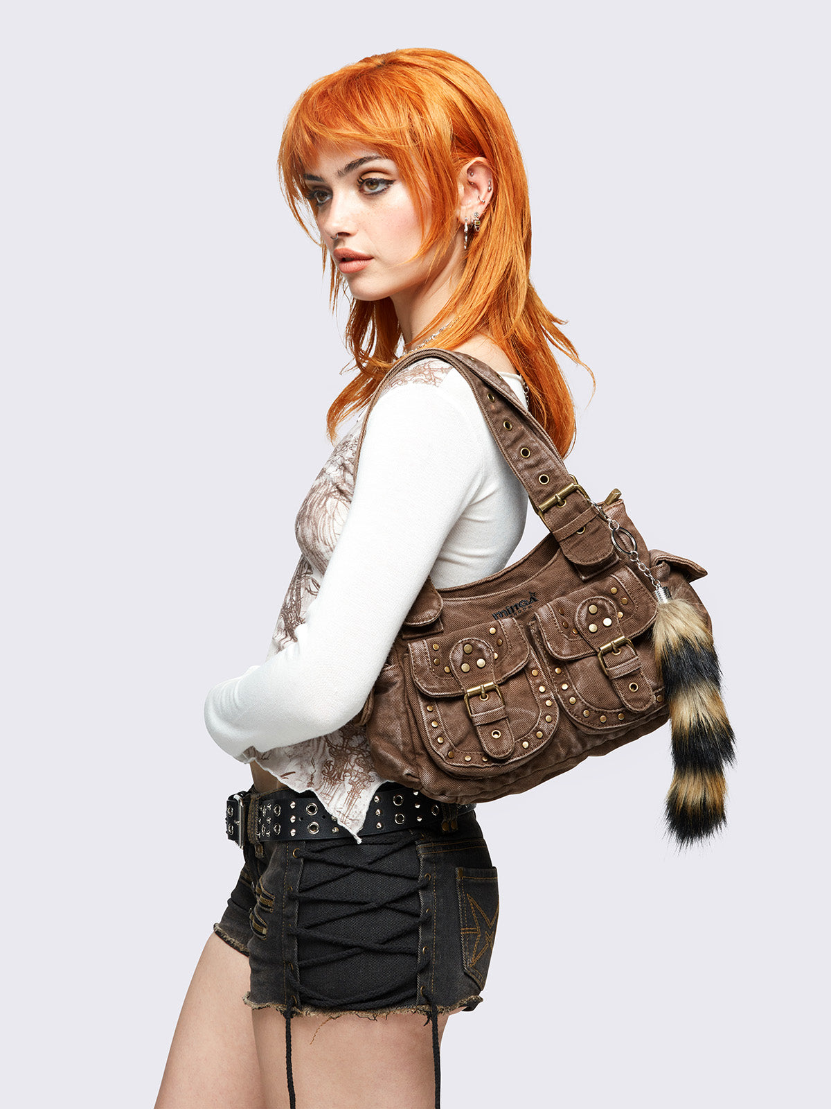 Brown washed denim buckle shoulder bag with removable faux fur fox tail keychain, multiple pockets and brass studs details.
