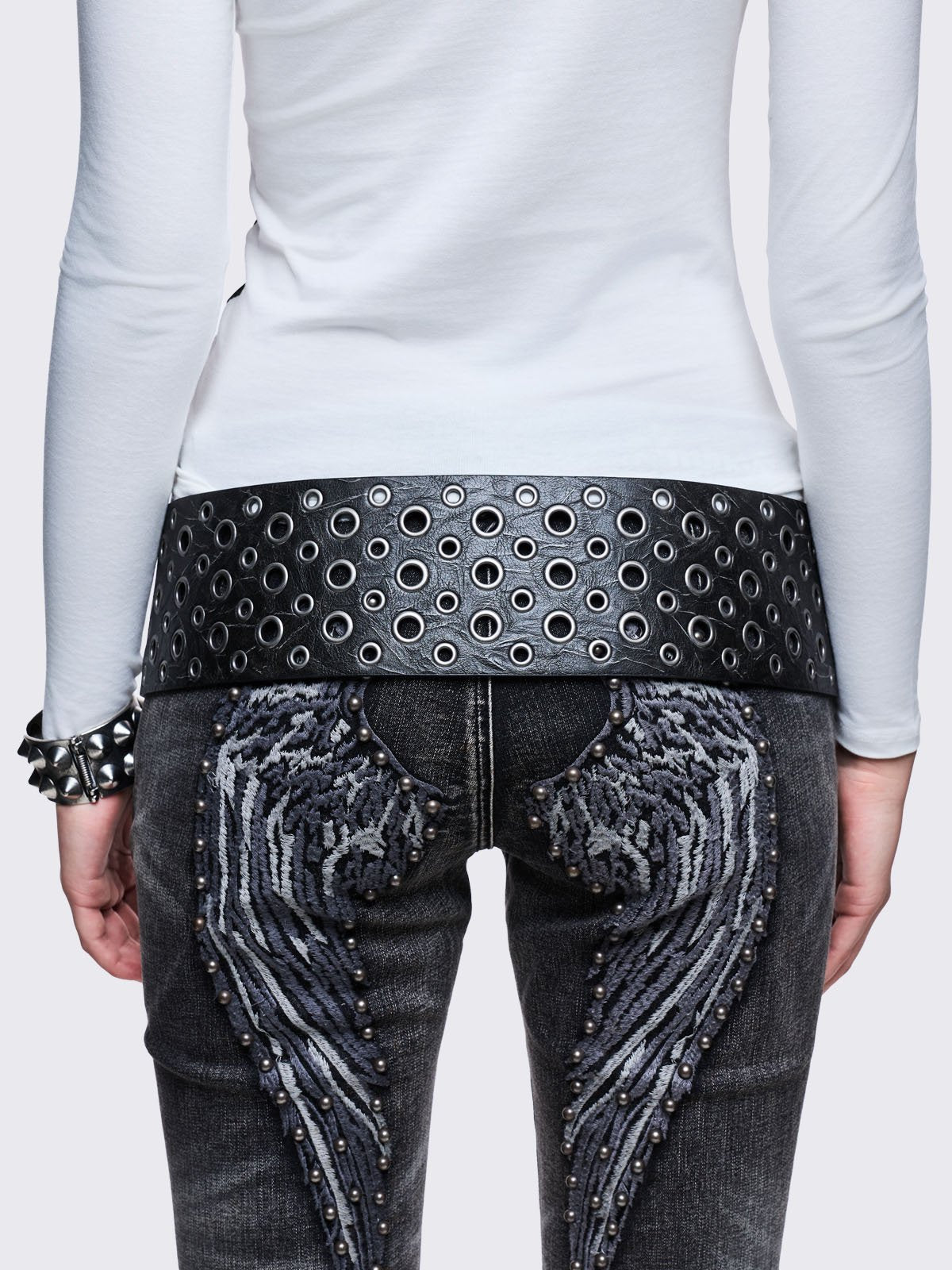 Wide black faux leather belt with multiple silver grommets/eyelets across the width, secured by a large triple-pin buckle, with a detachable star charm.