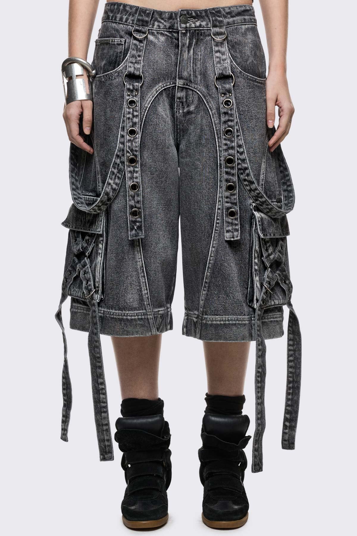 Grey washed denim jort with cargo pockets, eyelet straps, and metal hardware in an edgy grunge style.