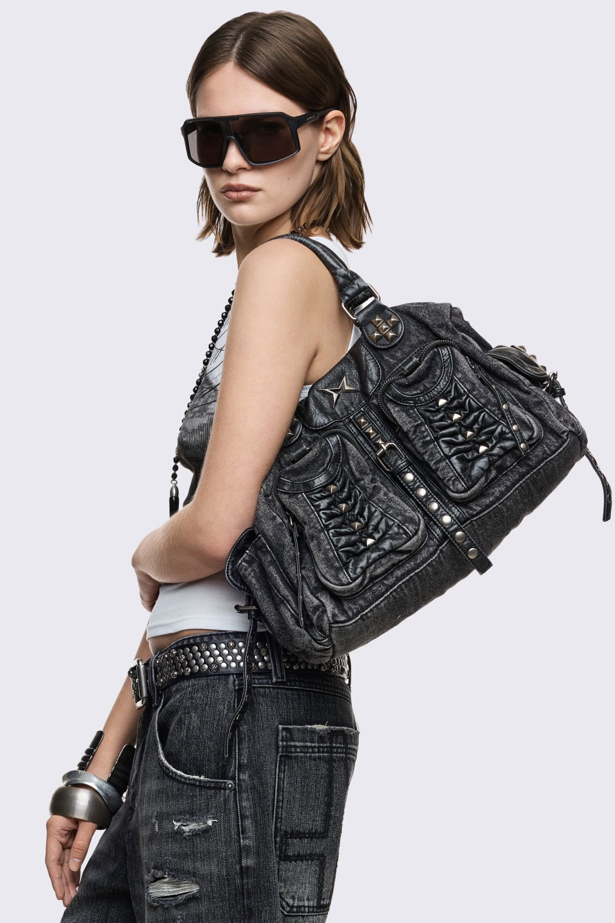 Black acid-wash denim shoulder bag with studs, ruched pockets and buckle details in a grunge Y2K style.