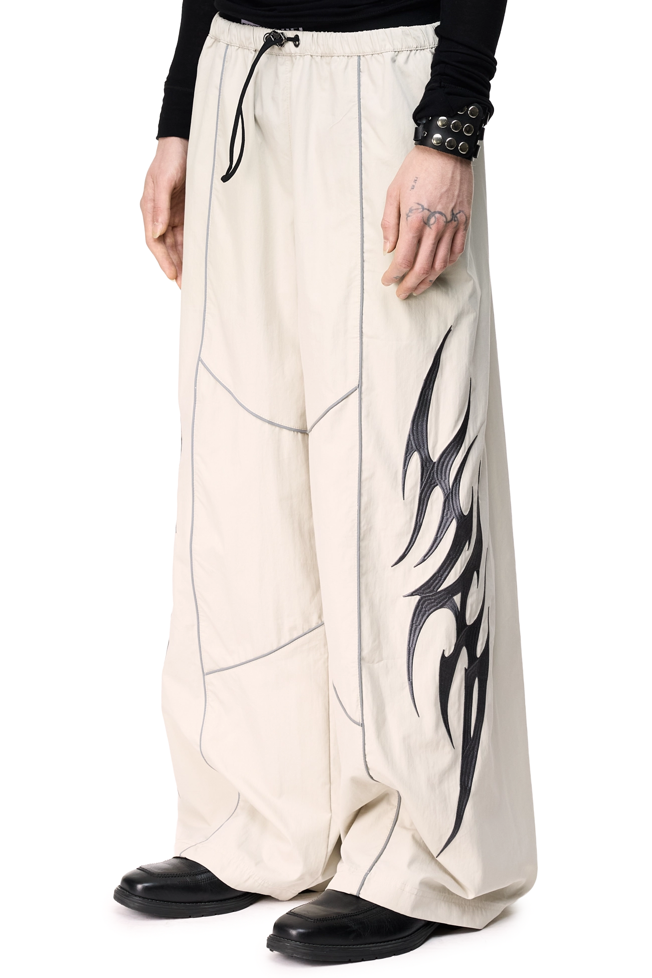Grey parachute pants with reflective piped seams, sigilism embroidery, side zip pockets and a wide leg fit.