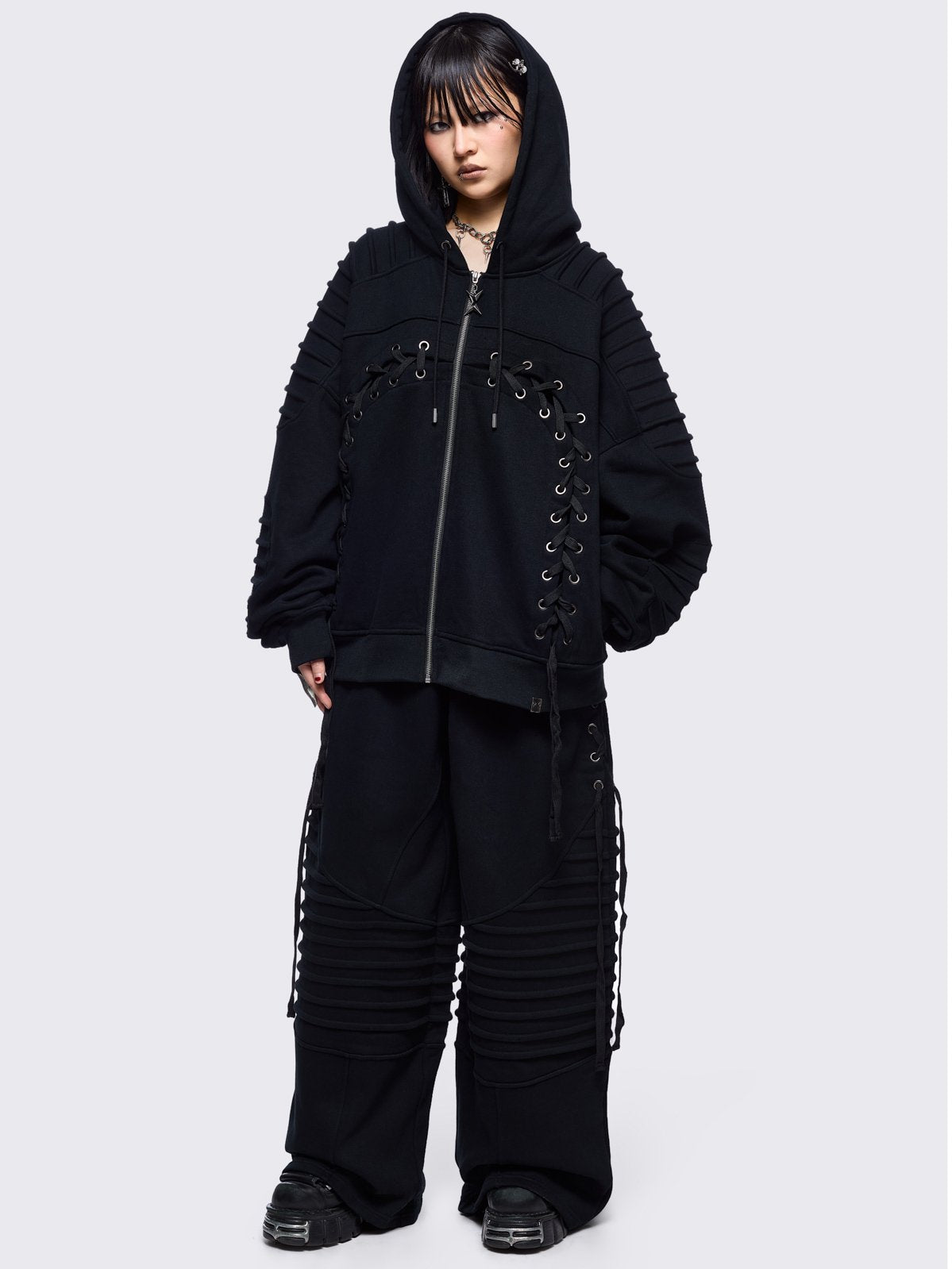 Black zip up hoodie jacket featuring a moto pintuck panels and front lace corset details. 