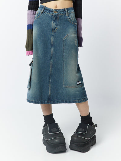 A 00s-inspired denim maxi cargo skirt named Kady by Minga London. This skirt combines the style of a cargo design with the length of a maxi skirt, creating a unique and fashionable look.