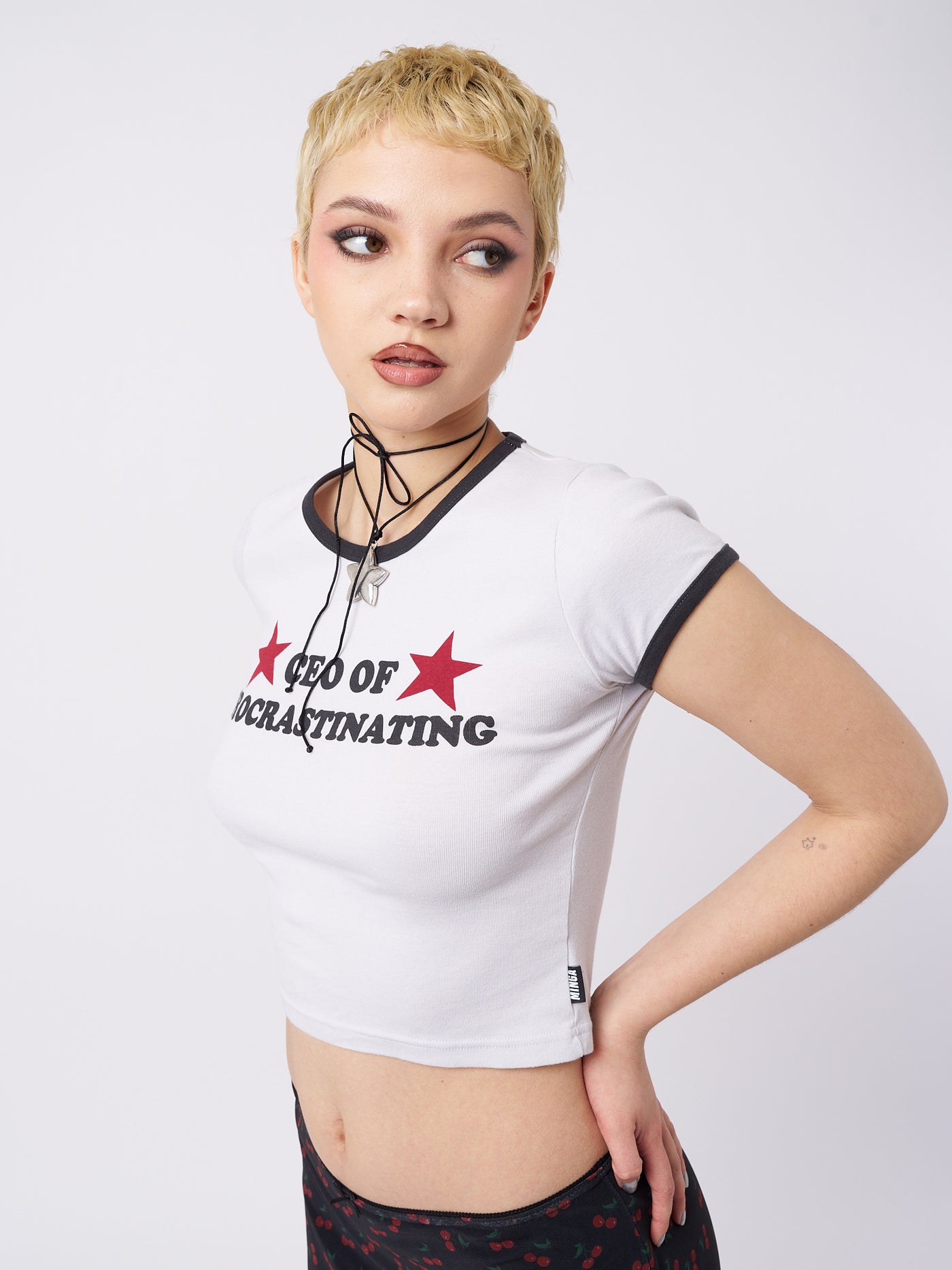 A baby tee with the text "CEO Of Procrastinating" by Minga London. This tee combines a playful and humorous design with a cool and casual style, perfect for expressing your laid-back and relatable personality.
